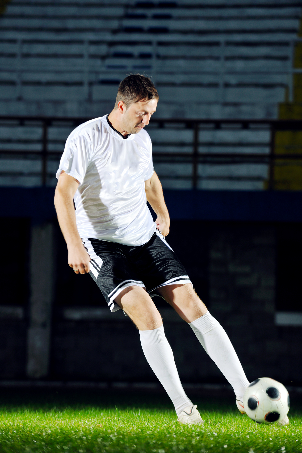 soccer player doing kick with ball on football stadium  field  isolated on black background  in night